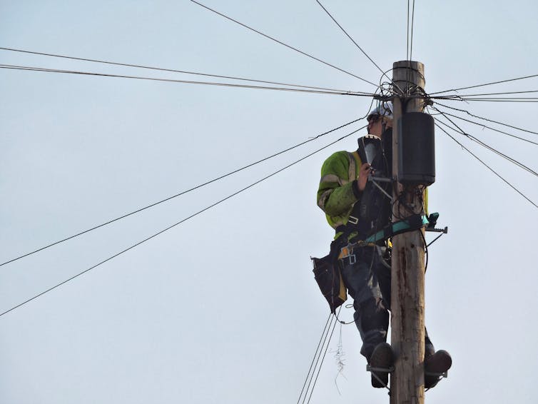 An engineer atop of wooden electricity transmission pole.
