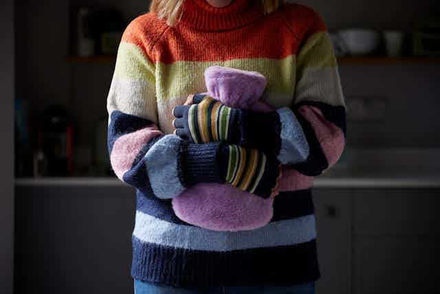 A woman in a colourful striped jumper wearing gloves and clutching a water bottle.