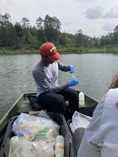 man seated in small boat wearing gloves injecting water into a collection tube