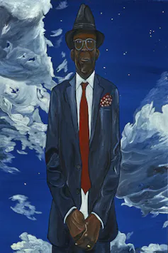 A tall Black man against a cloudy sky, wearing a fedora hat.