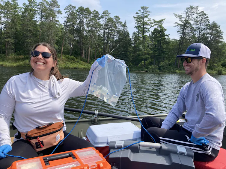 woman holds a clear plastic bag aloft, she and man are seated in boat