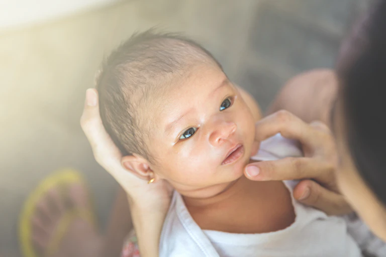 A baby gazing with an adult hand cradiling their head.