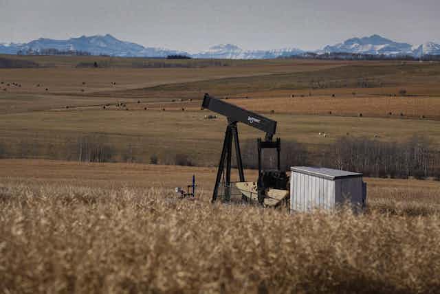 A decomissioned pumpjack seen in a field against a backdrop of mountains.