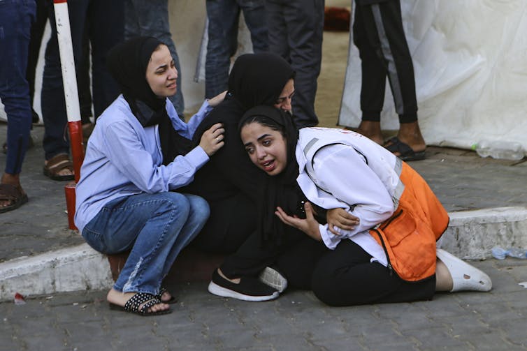 Three young women wearing hijabs crying by the side of a road