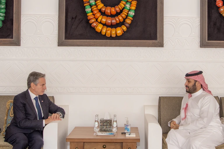 A man in a suit talks to a man in traditional Saudi dress separated by a table.
