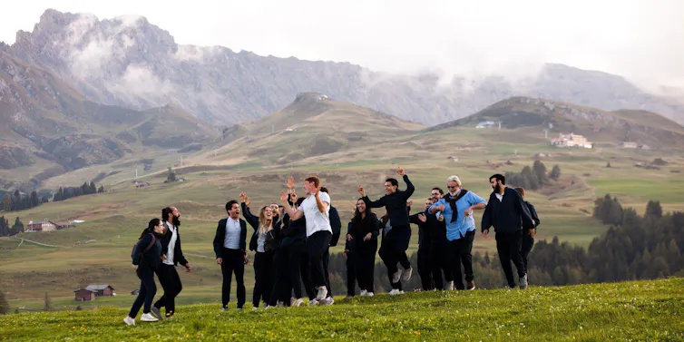 Un grupo de jóvenes salta y ríe en una pradera en el monte.
