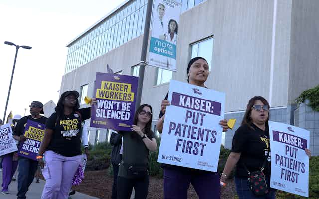 People march, carrying signs saying things like 'Kaiser workers won't be silenced' and 'Kaiser, put patients first.'