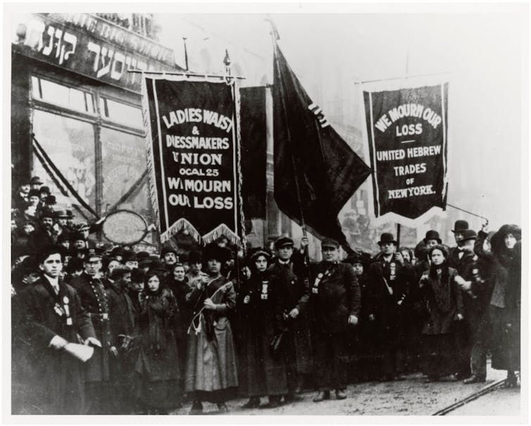 A black and white photograph of a crowd of women in long coats, holding banners that say 'We mourn our loss.'