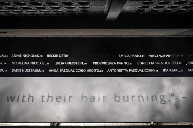 A metal inscription on a steel building lists around a dozen names, plus part of a larger quote: 'with their hair burning.'