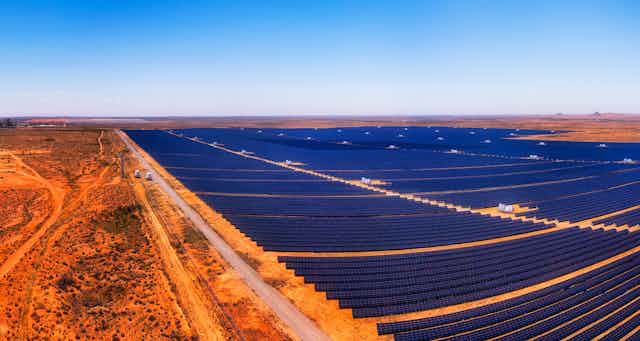 A zoomed out panorama of a large solar farm surrounded by red soil