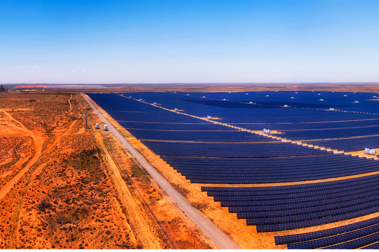 A zoomed out panorama of a large solar farm surrounded by red soil