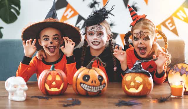 Three children dressed up for Halloween smile at the camera