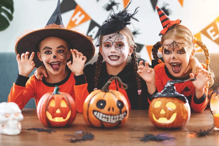 Three children dressed up for Halloween smile at the camera