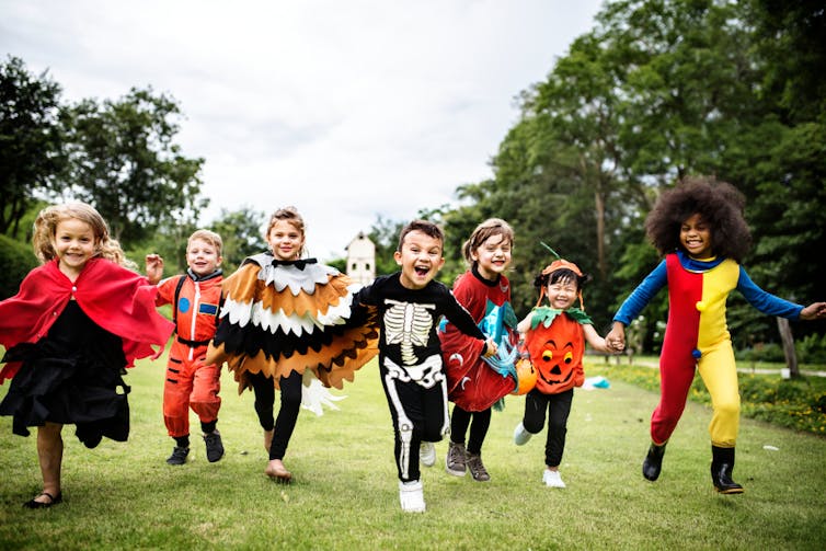 A group of small children in Halloween costumes run towards the camera smiling