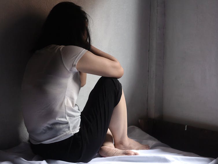 woman sits on bed facing wall to hide face