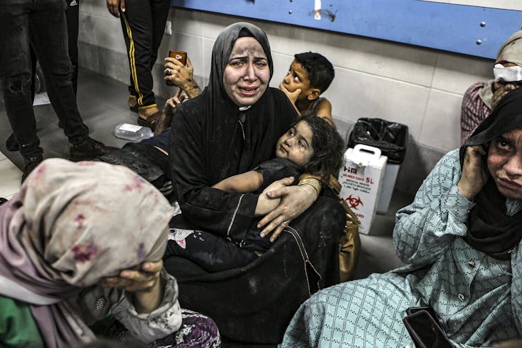 A crying woman in a hijab holds a young child in her arms in a hospital.