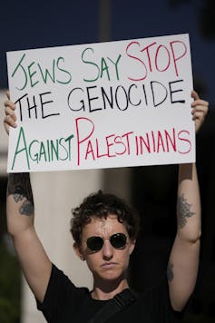 A woman holds a placard reading: Jews say stop the genocide against Palestinians