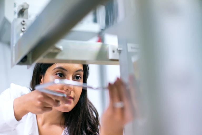 A woman in a lab coat works with a machine.