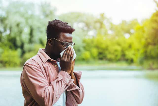 A man with hay fever blows his nose into a tissue.