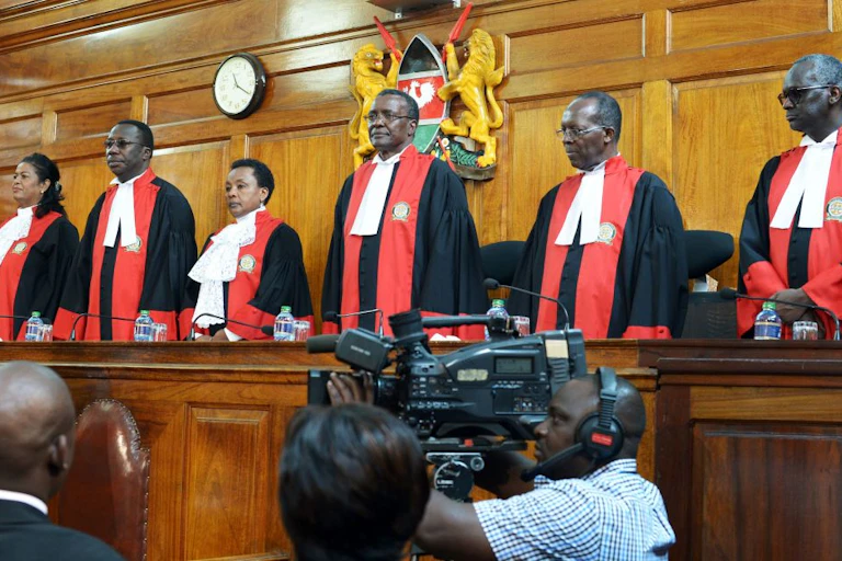 Four men and two women dressed in red and black robes standing behind a wooden platform
