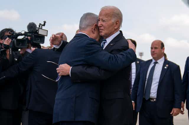 Two men in suits hug on an airport tarmac.