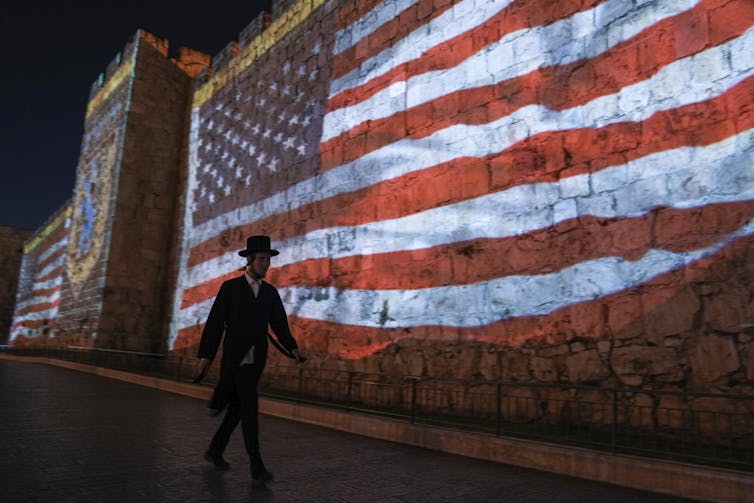 A man in a hat walks past a giant American flag.