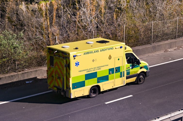 A yellow ambulance driving down a road.