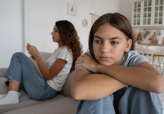A teen sitting near a parent hunched over her knees.