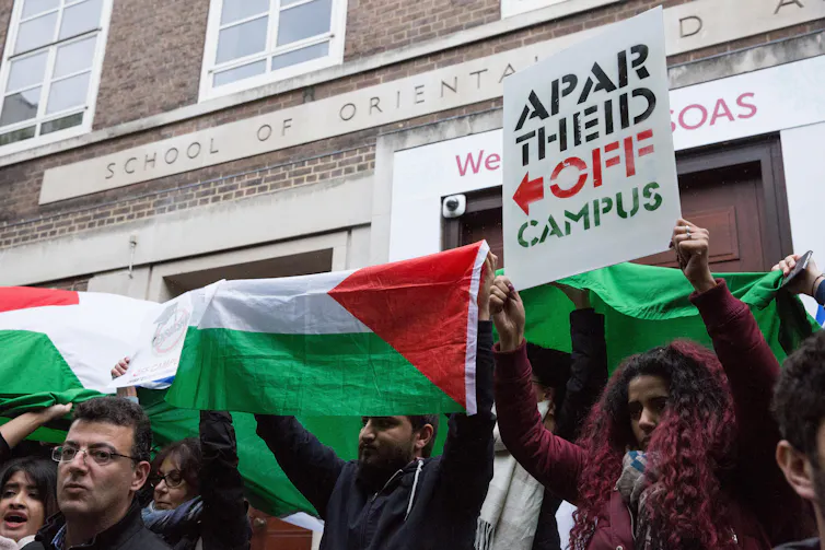 Students holding Palestinian flags and a sign reading Apartheid off campus.