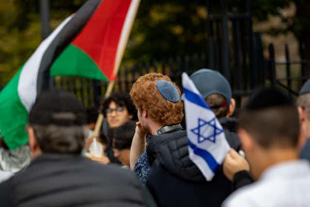 A crowd of protesting university students, one Israeli flag and one Palestinian flag are visible