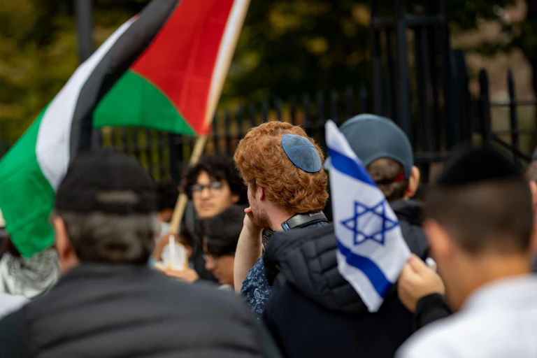 A crowd of protesting university students, one Israeli flag and one Palestinian flag are visible