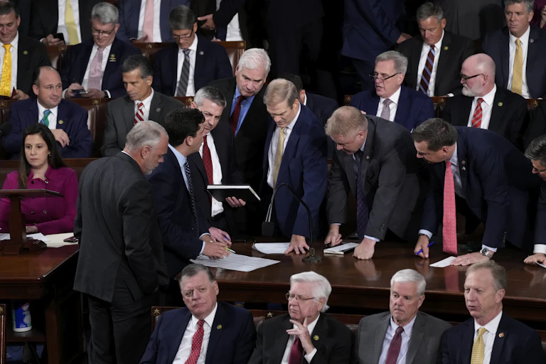Men in suits stand around a desk, looking at papers.