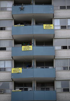 A high-rise with balconies, some with signs that read: 'stop raising rents.'