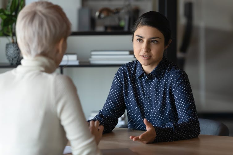 Two women having a serious conversation at a table. One of the women has her back to the camera.