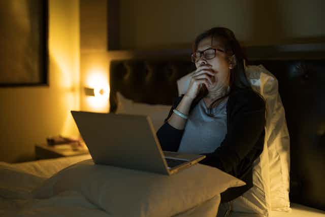 Yawning woman using laptop in bed