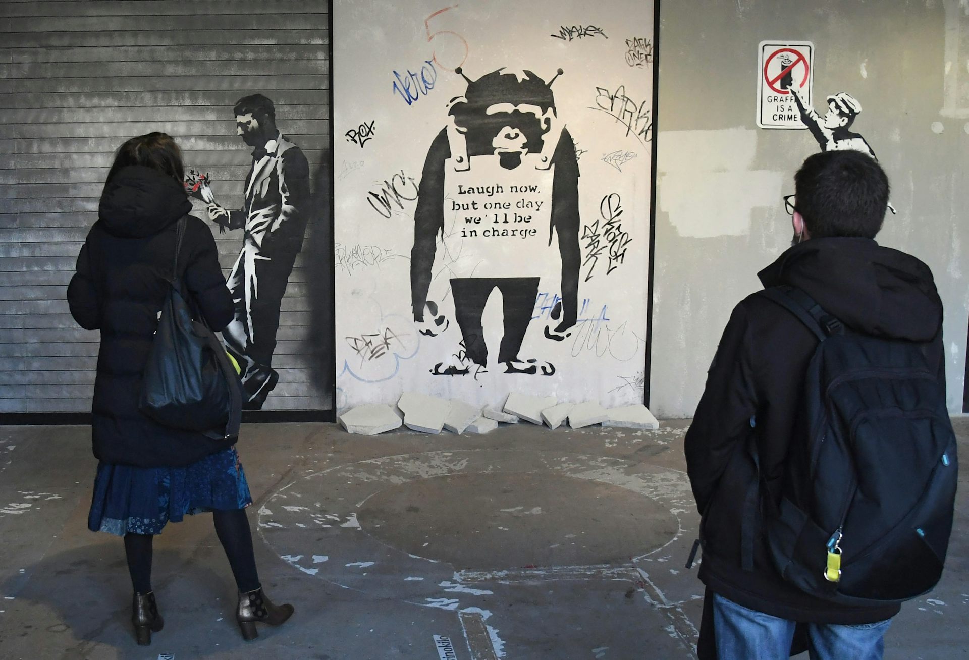 Duas pessoas olham para a obra de arte de Banksy sobre um macaco