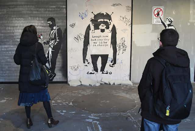 Duas pessoas olham para a obra de arte de Banksy sobre um macaco