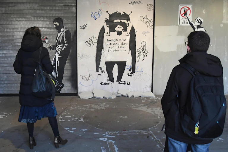Duas pessoas olham para a obra de arte de Banksy sobre um macaco