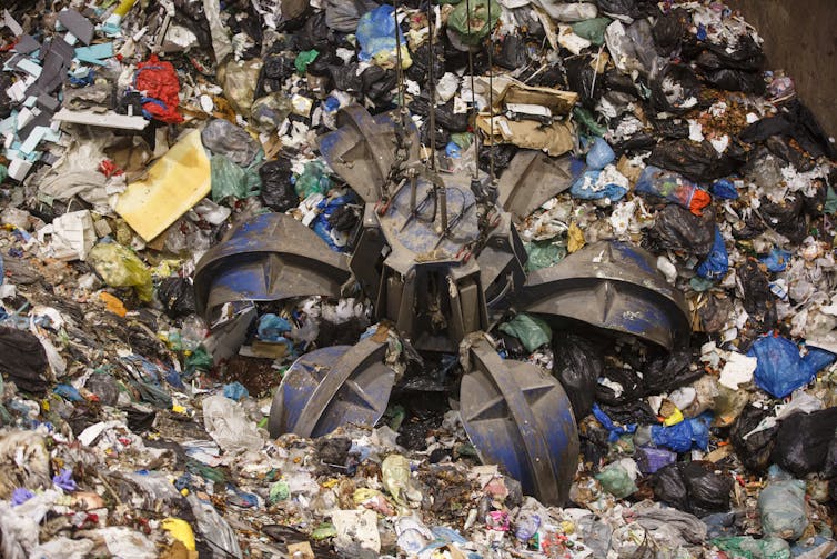 A mechanical claw grabbing pile of mixed plastics at a waste treatment plant.