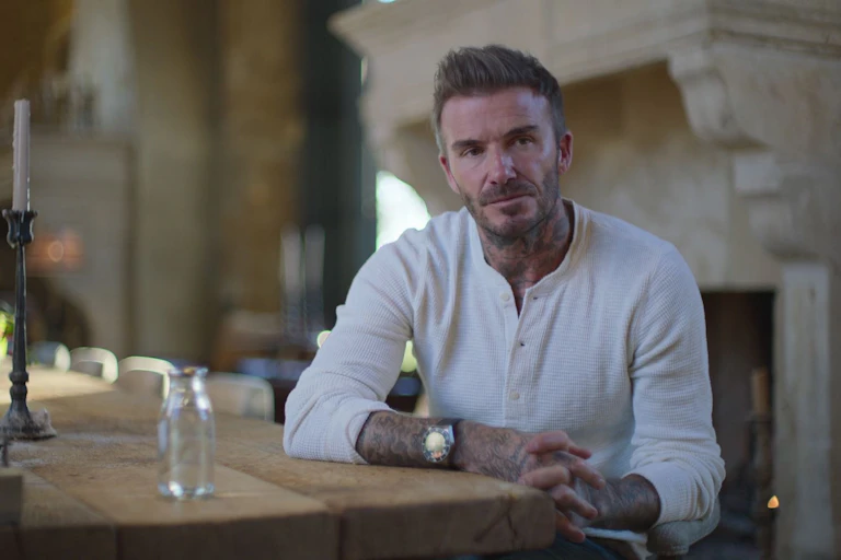 A man in a white top sits at a table and looks into the distance