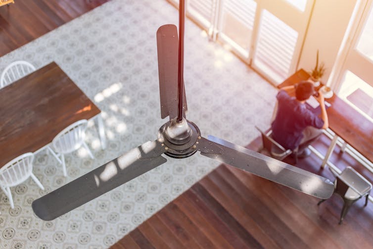 Looking down from the top of a room at a ceiling fan and man sitting at a desk