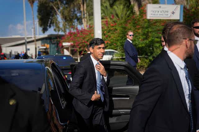 Rishi Sunak getting out of a car with many bodyguards around him.