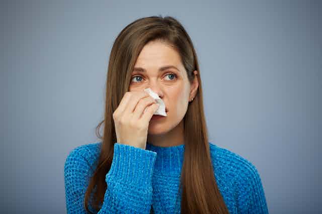 Woman holding a tissue to her nose.