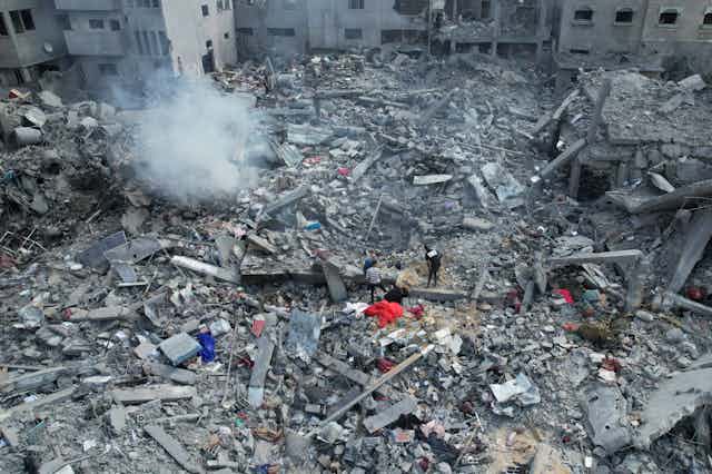 A smoking pile of rubble, with people searching for survivors amid the debris.
