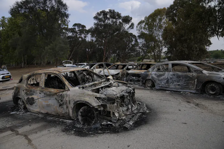 Destroyed, burnt-out cars in a dusty parking lot.