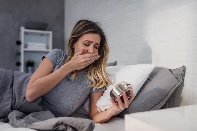 A tired woman looks at her alarm clock.
