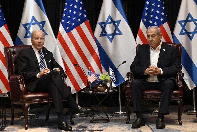 Joe Biden sits next to Benjamin Netanyahu, behind a row of Israel and US flags.