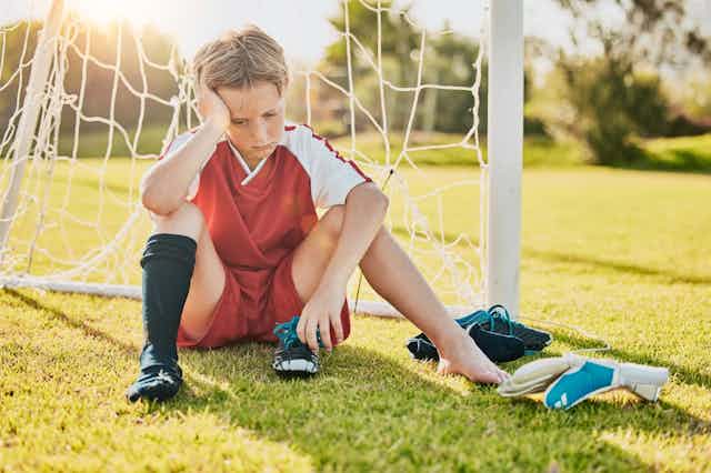 A boy sitting on a soccer pitch looking sad