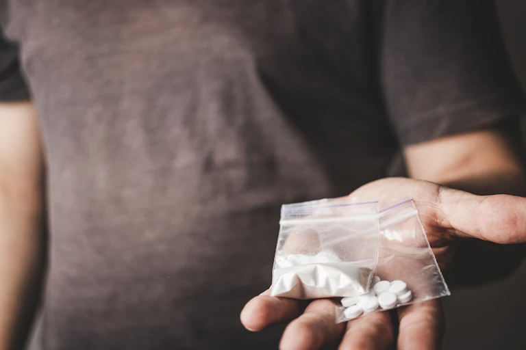 An outstretched hand holding powder in one clear packet and pills in another.