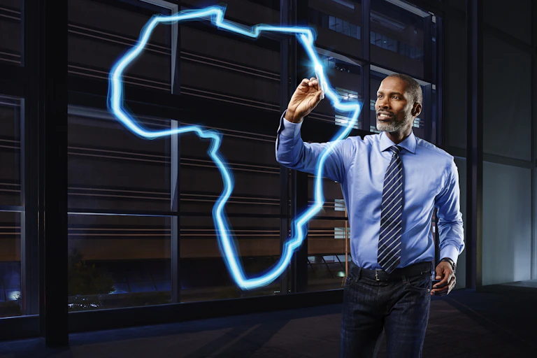 A photograph of a businessman in a light blue shirt and a dark blue striped tie painting a map of the African continent in light